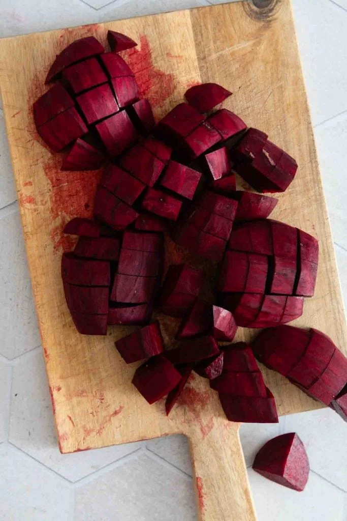Auf einem Holzbrett liegen in Würfel geschnittene Rote Bete Knollen.