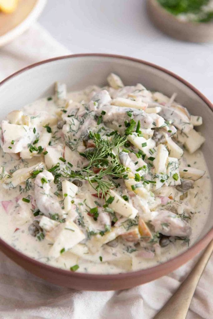 heringssalat hausfrauenart nach omas rezept in einer Keramik-Servierschüssel dekoriert mit Kräutern