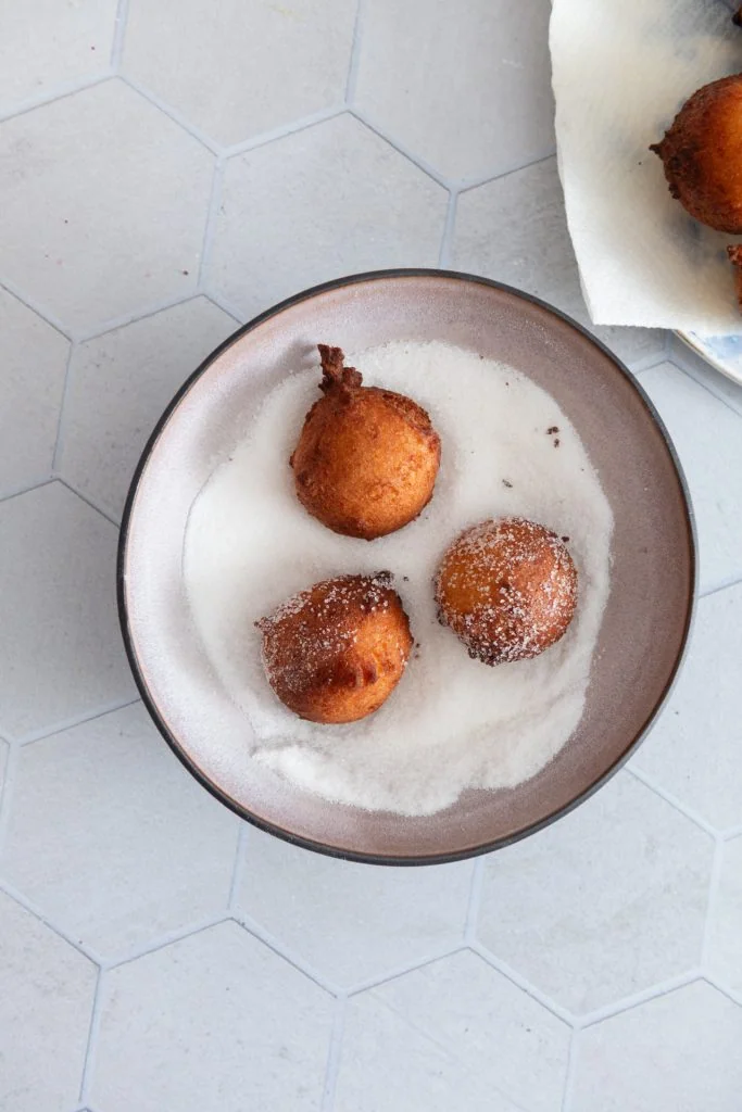 Drei Quarkbällchen werden in einer Schüssel mit Zucker gewälzt.