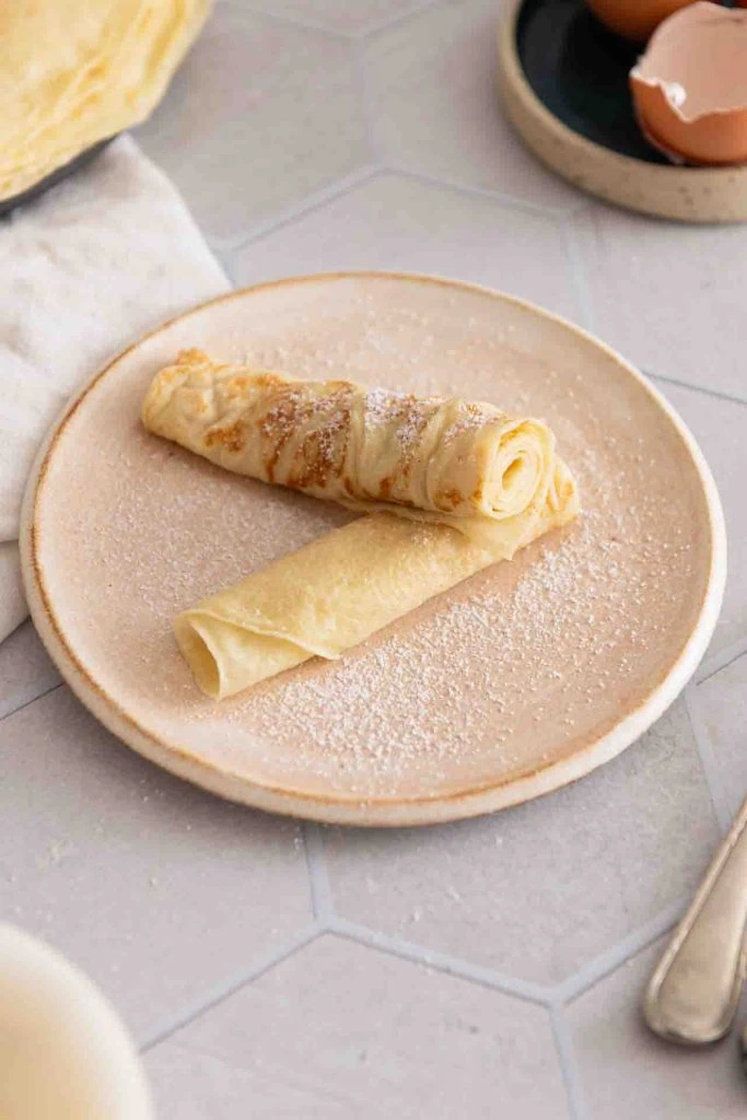 Ein Pfannkuchen zusammengerollt und halbiert mit Puderzucker.