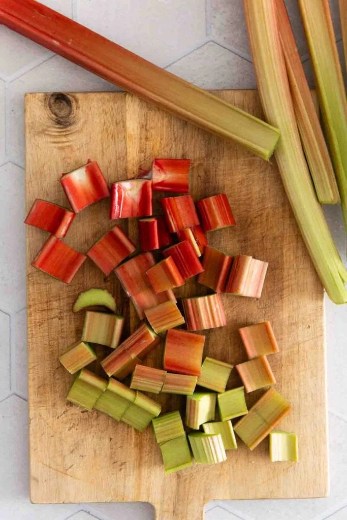 In Stücke geschnittene Rhabarberstangen liegen auf einem Holzbrett. Am oberen Rand des Bildes sind weitere, ganze Spargelstangen zu sehen.
