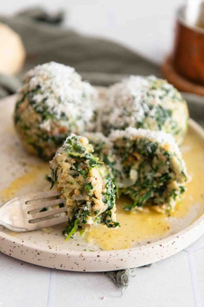 Eine Gabel nimmt etwas von den Spinatknödel auf.