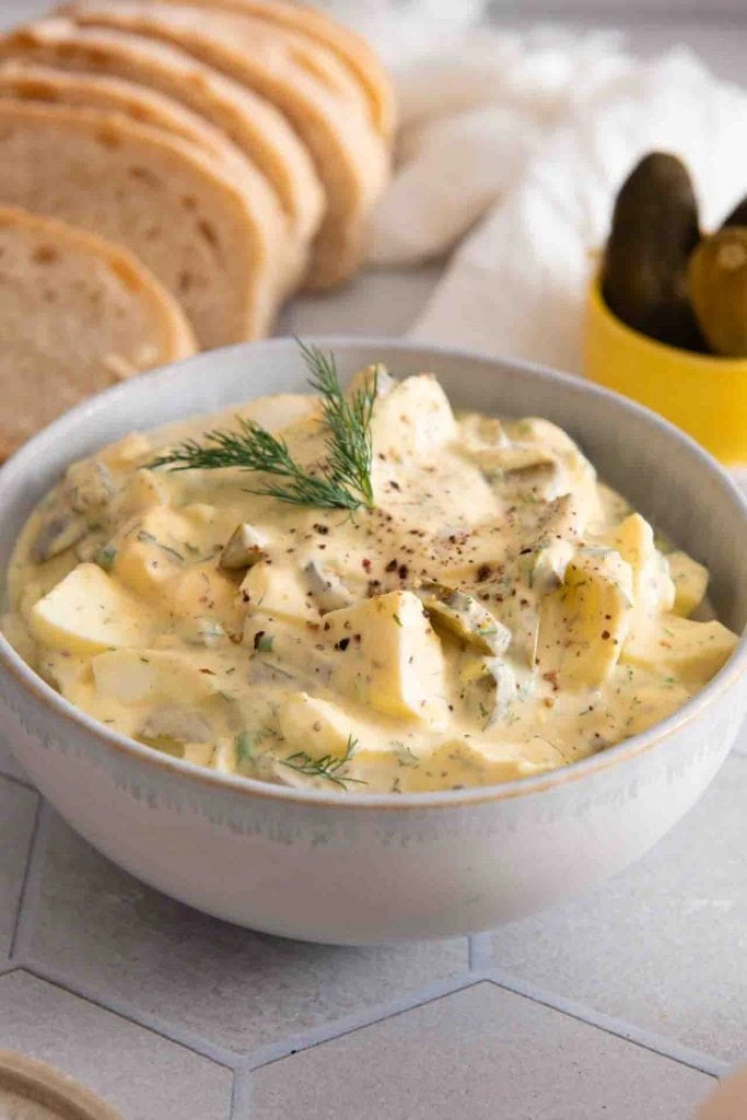 Der fertige Eiersalat in einer Schüssel mit Brot und Gurken.