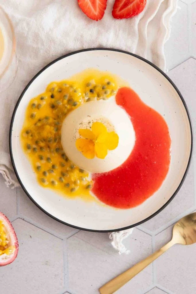 Maracuja und Erdbeersauce sind neben dem Panna Cotta auf dem Teller.