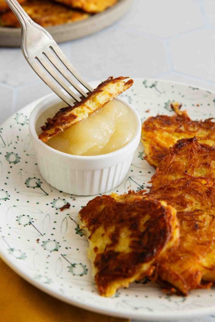 Eine Gabel taucht den Kartoffelpuffer in das Apfelmus ein.